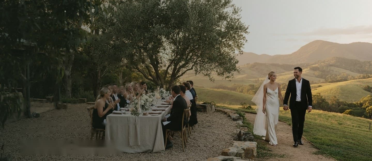 A couple walking beside a long outdoor wedding table in the hinterland at golden hour